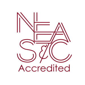 The image is of a shield with a blue and white background. In the center of the shield is a gold star. Above the star is the word "NEASC", and below the star is the word "accredited".